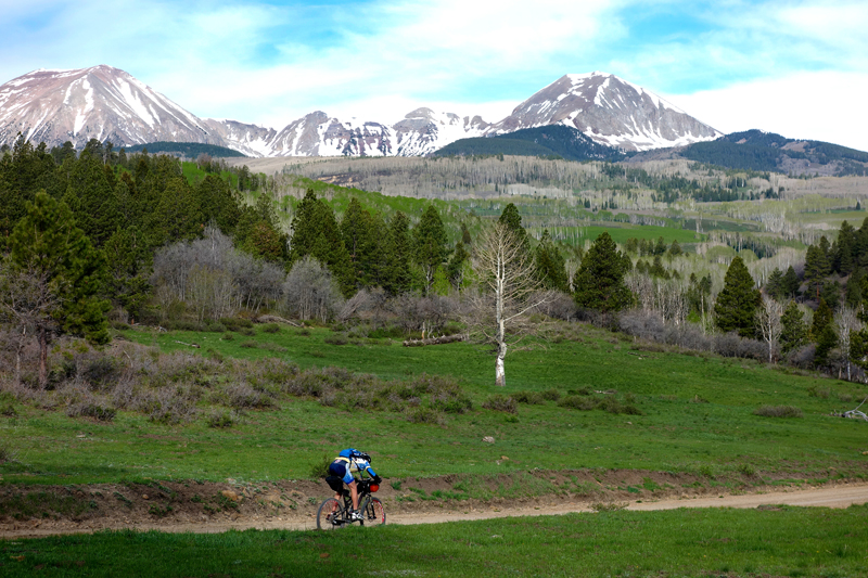 Ty Hopkins riding on 2 Mile Road with the La Sals in the background. La Sal Peak is on the right.